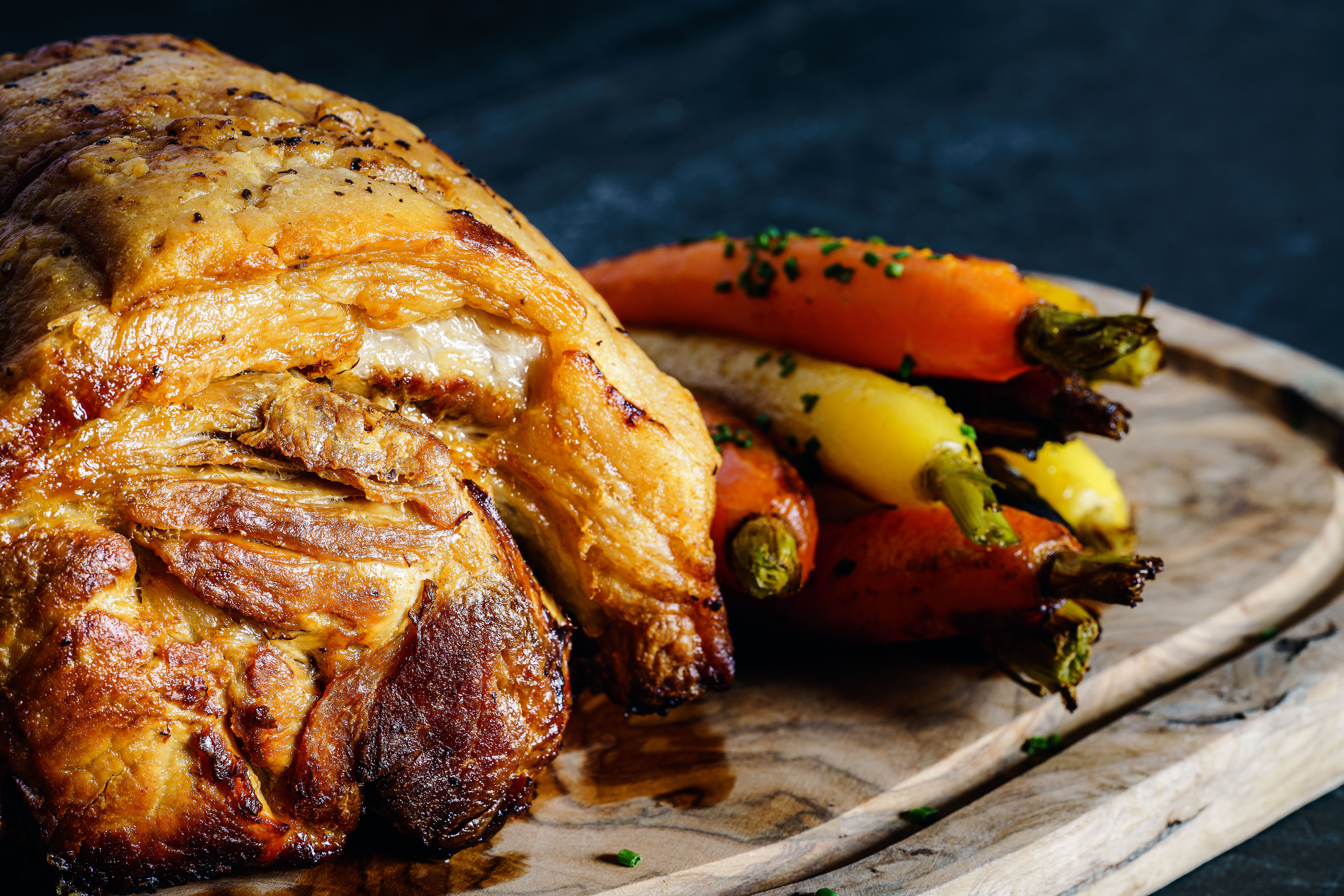 Delicious roast pork served with colorful carrots on a wooden board.