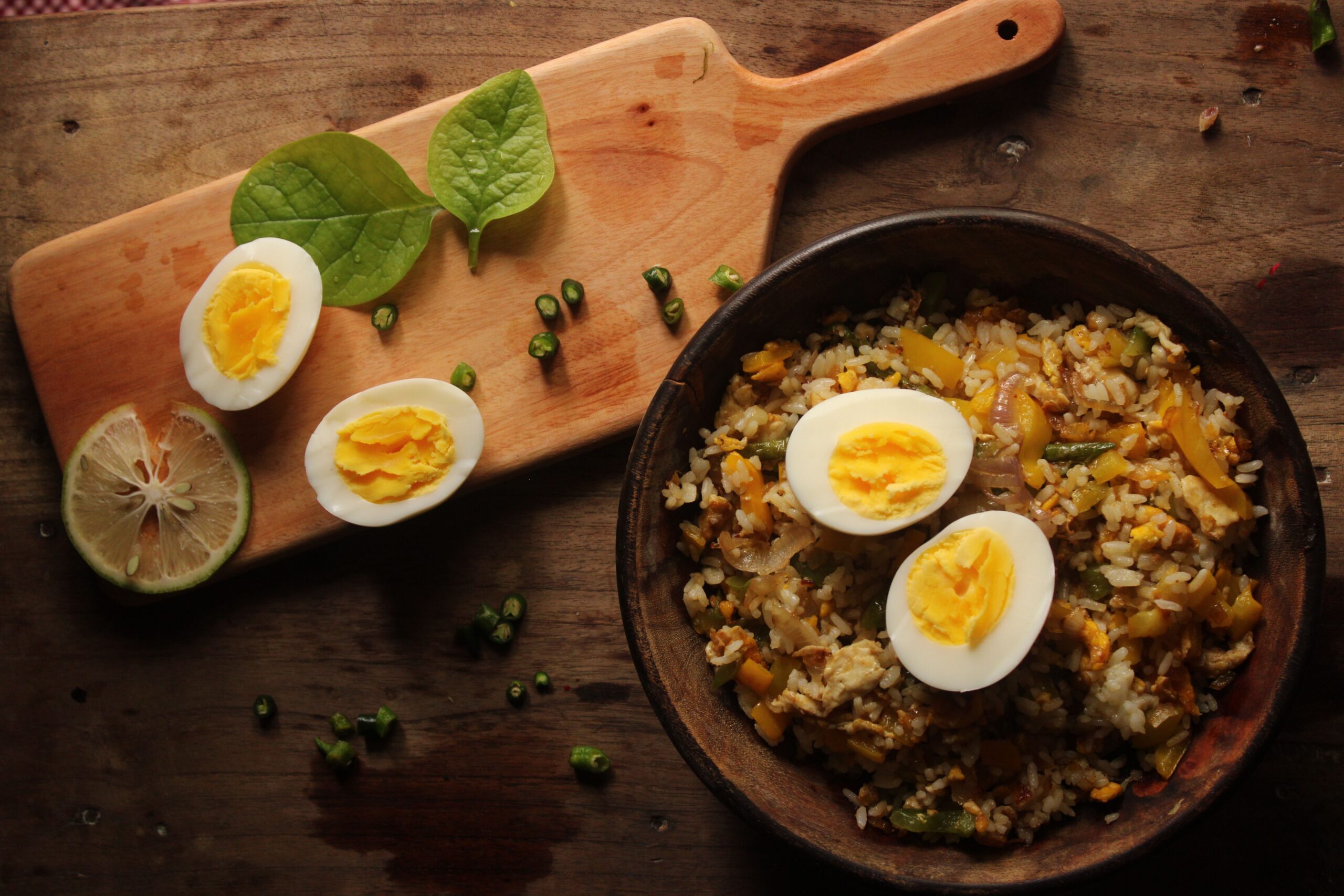 Top-down view of a bowl of fried rice with eggs and greens on a wooden board.