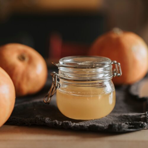 Homemade pumpkin spice syrup in a glass jar beside small pumpkins