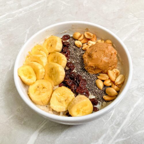 Bowl of overnight oats topped with banana slices, peanuts and peanut butter