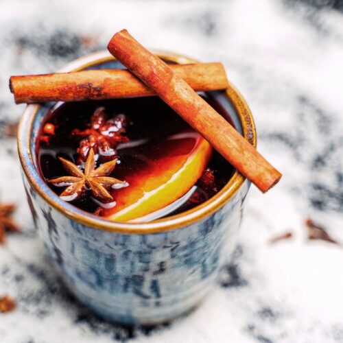 Mug of slow cooker mulled red wine punch garnished with cinnamon sticks, star anise and an orange slice