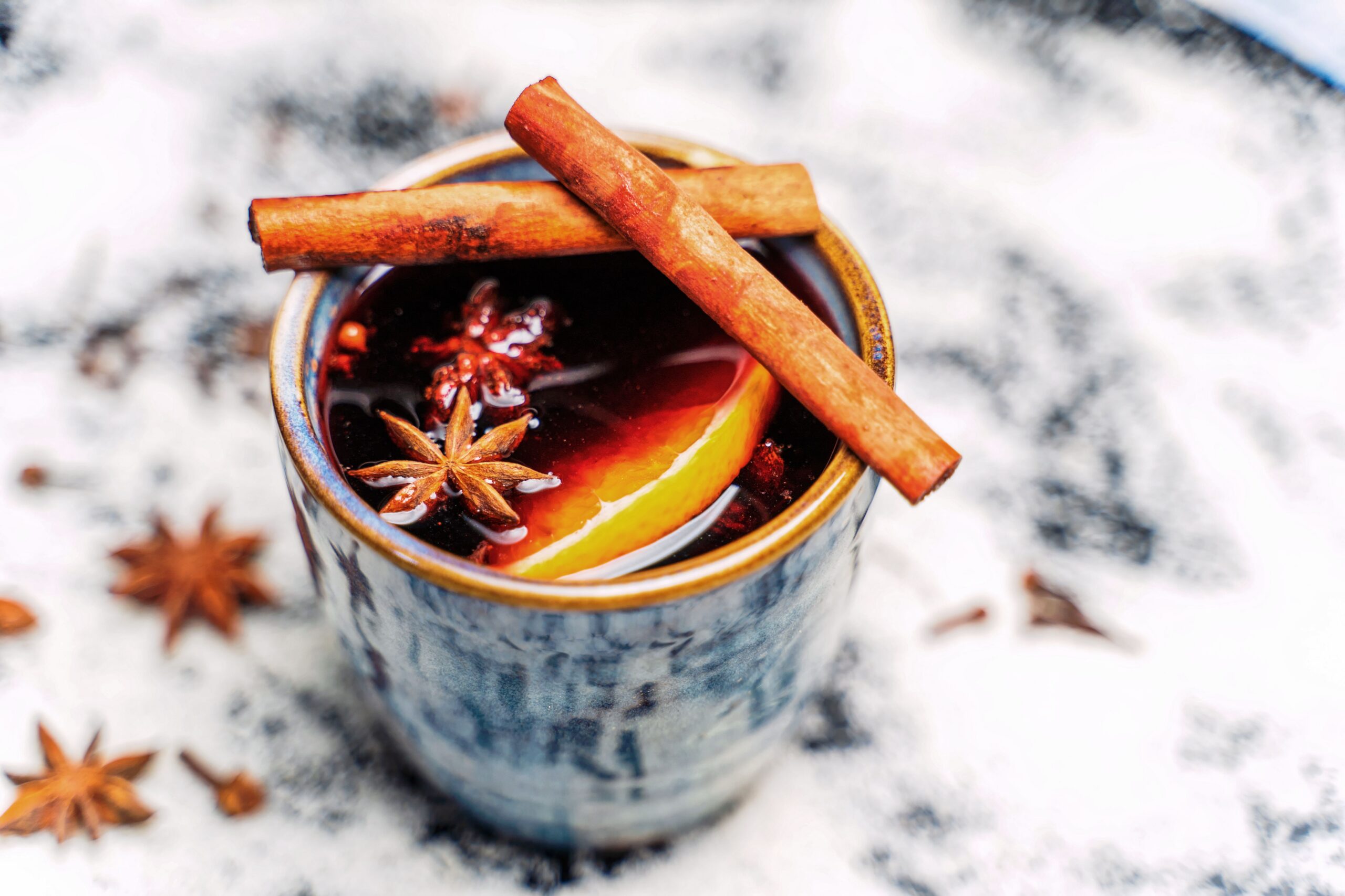 Mug of slow cooker mulled red wine punch garnished with cinnamon sticks, star anise and an orange slice