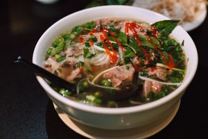 Delicious bowl of traditional Vietnamese pho garnished with fresh herbs and spicy sauce.