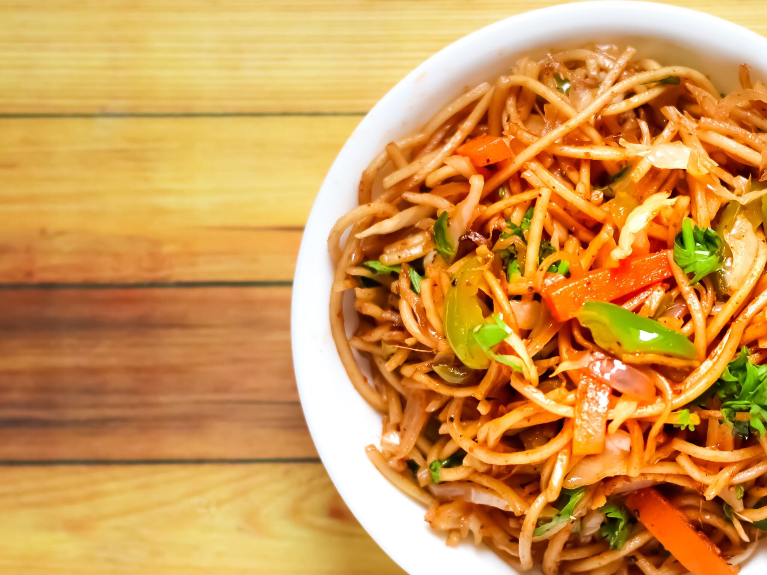 A vibrant bowl of spicy Indian noodles garnished with vegetables on a wooden table.