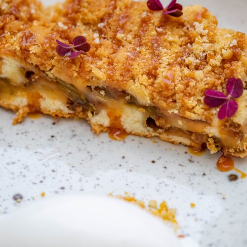 A close-up of apple crisp with a golden oat crumble topping and cream.