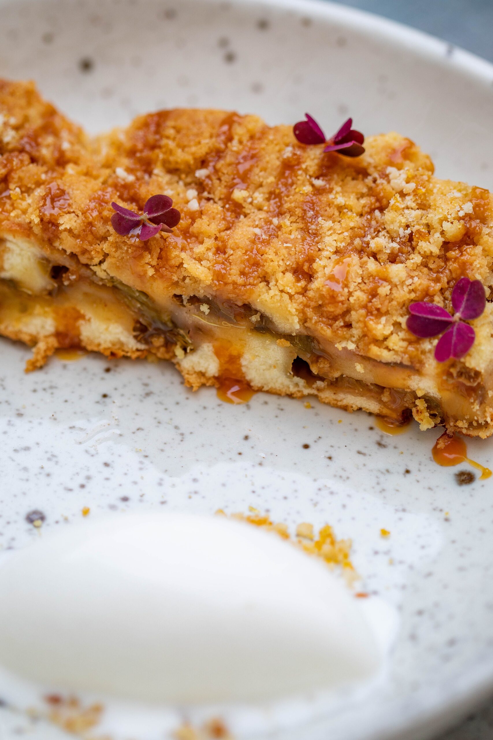 A close-up of apple crisp with a golden oat crumble topping and cream.
