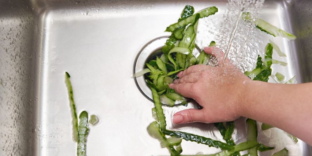 A hand pushing down vegetable peelings through a sink.