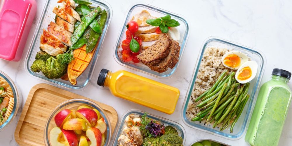Flat lay shot of glass food containers with an assortment of prepared meals made through meal planning on a budget.