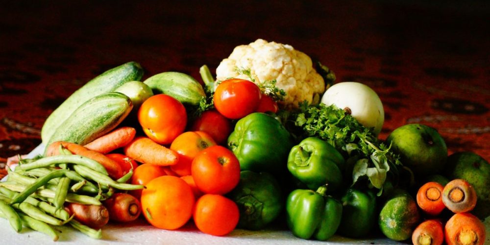 Tomatoes, bell peppers, carrots, cauliflower, and other vegetables piled together on a table.