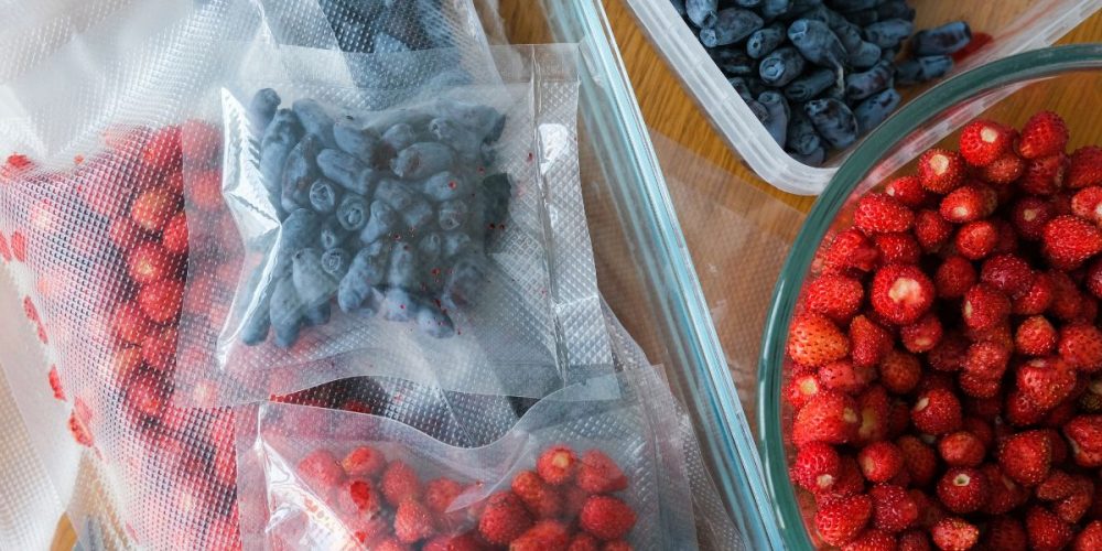 strawberries and blueberries in separate vacuum bags beside a big bowl of strawberries.