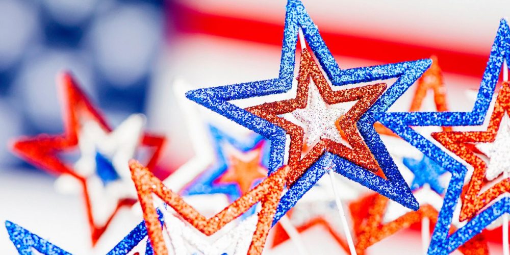 Focus shot on glittery stars in red, white and blue with the American flag just behind it.