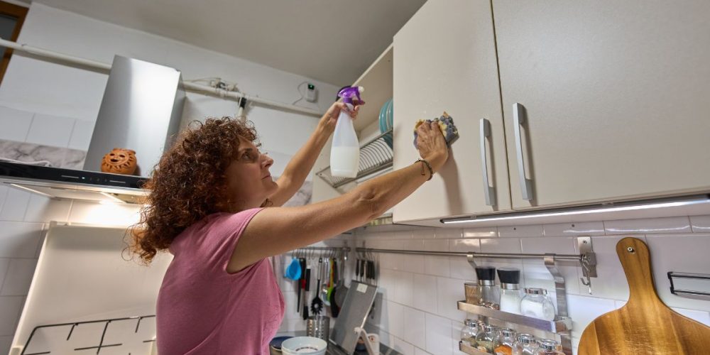 A woman wiping her kitchen cupboards clean.