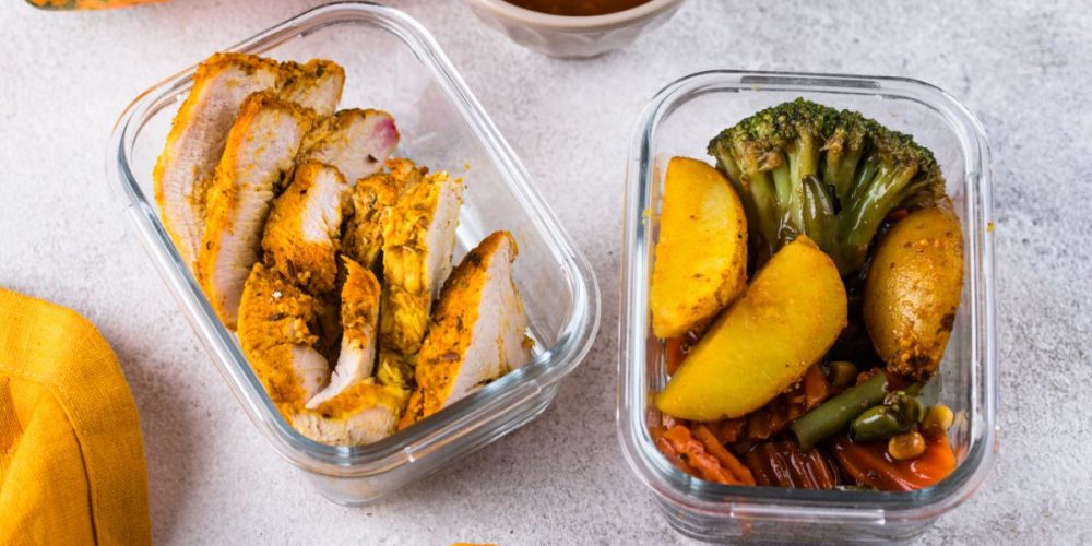 two glass containers, one with roasted chicken and the other with roasted vegetables, on a kitchen countertop.