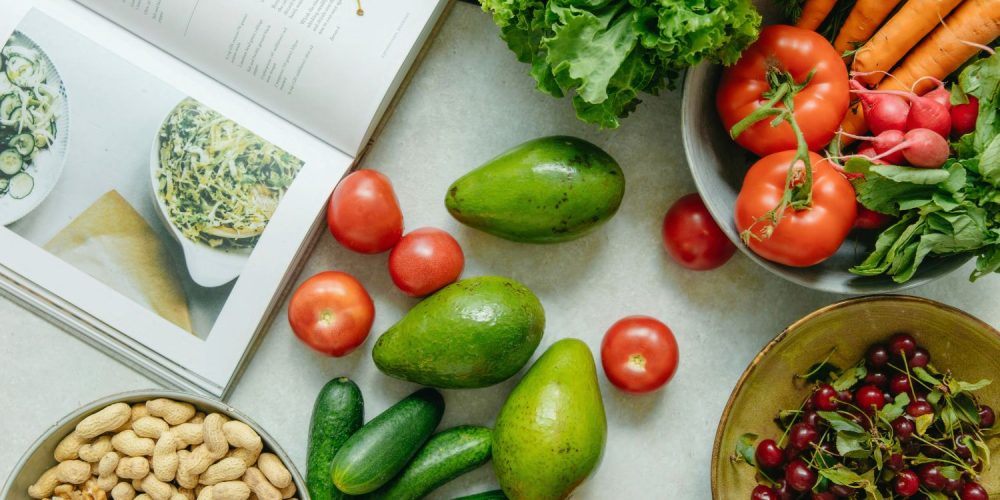 Flat lay shot of vegetables and a cookbook on a white surface.
