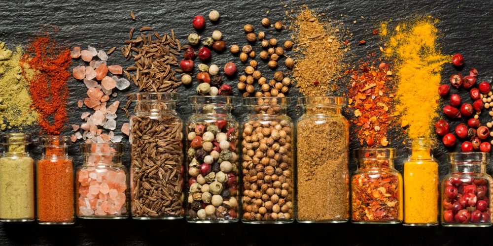 Flat lay shot of spice bottles each with spices on each of them, on a gray surface.