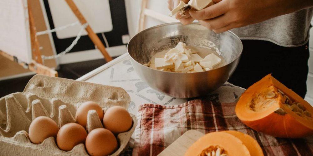 A person cutting butter into a mixing bowl for baking.