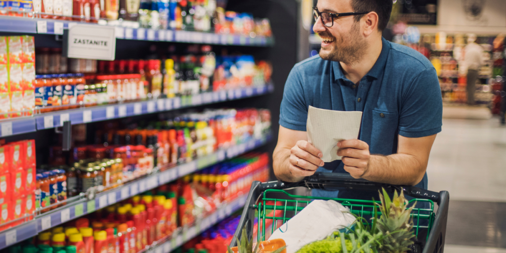 A man walking through a grocery isle while pushing his cart.