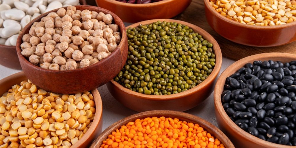 An assortment of dried beans in individual wooden bowls.