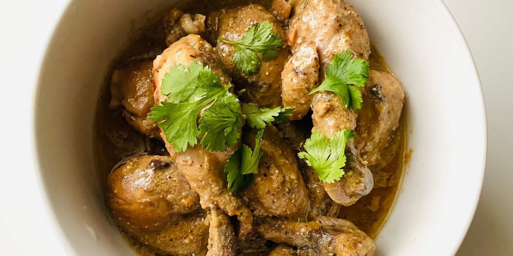 Bone-in chicken drumsticks and thighs braised in adobo sauce, served in a white bowl and garnished with fresh cilantro.