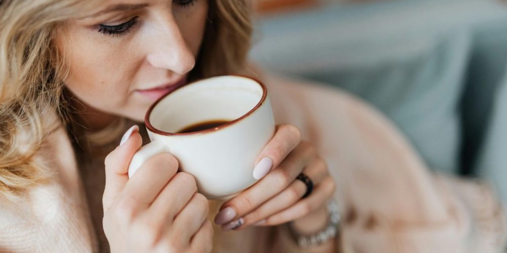 A woman drinking black coffee in a white mug.