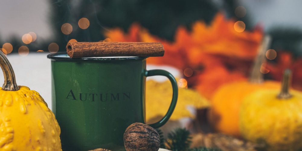 Fall spiced coffee in a green enamel mug with a cinnamon stick, surrounded by pumpkins