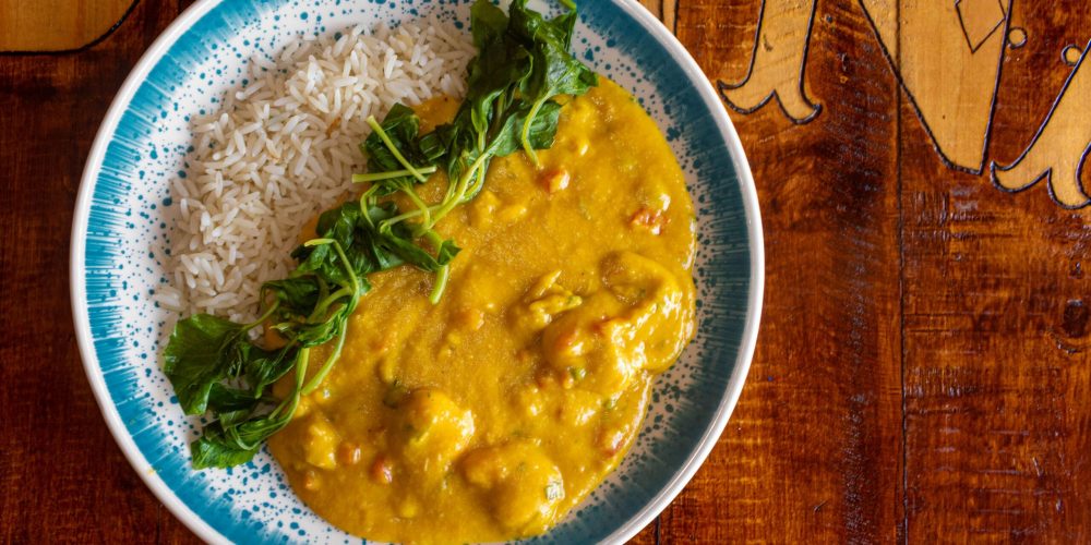 Close-up of curry dish with rice and greens on a wooden table, perfect for food photography.