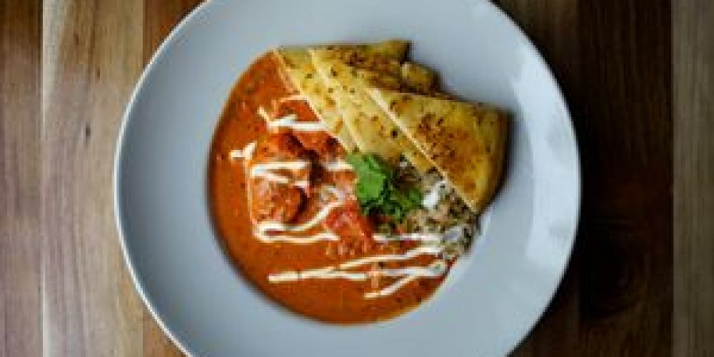 Top view of a flavorful butter chicken dish served with naan and garnished with cilantro.