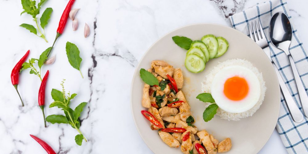 Delicious Thai basil chicken with rice and fried egg, styled on marble.