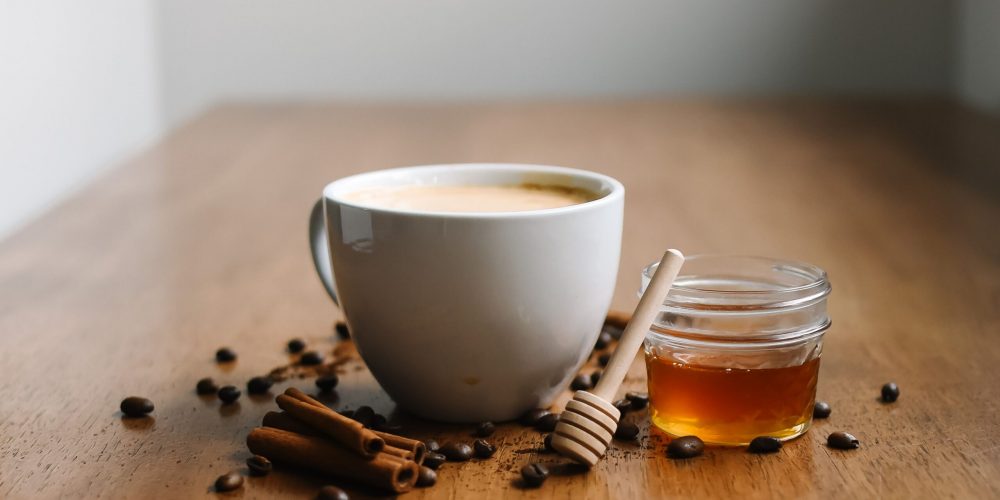 Chai latte made from homemade chai concentrate, in a white cup with cinnamon sticks and honey