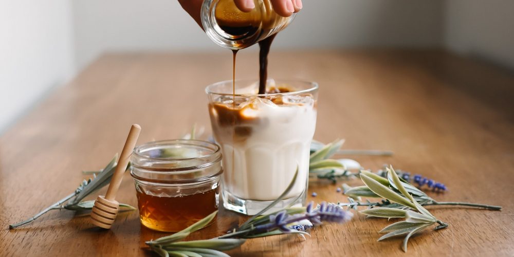 Coffee poured over homemade maple vanilla creamer in a glass, with a jar of honey alongside