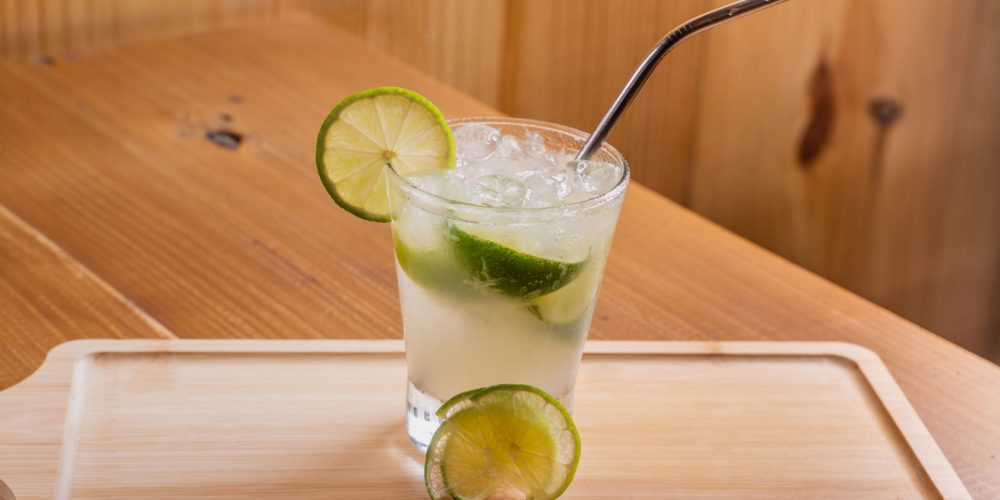 Tall citrus highball over ice with lime wheels, served on a wooden tray