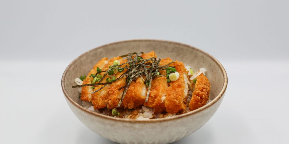 A mouthwatering chicken katsu served on steamed rice with savory toppings in a bowl.