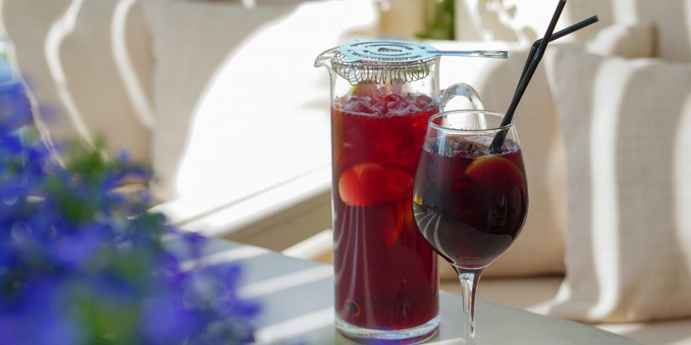 Pitcher and glass of deep red cranberry pear sangria on an outdoor table