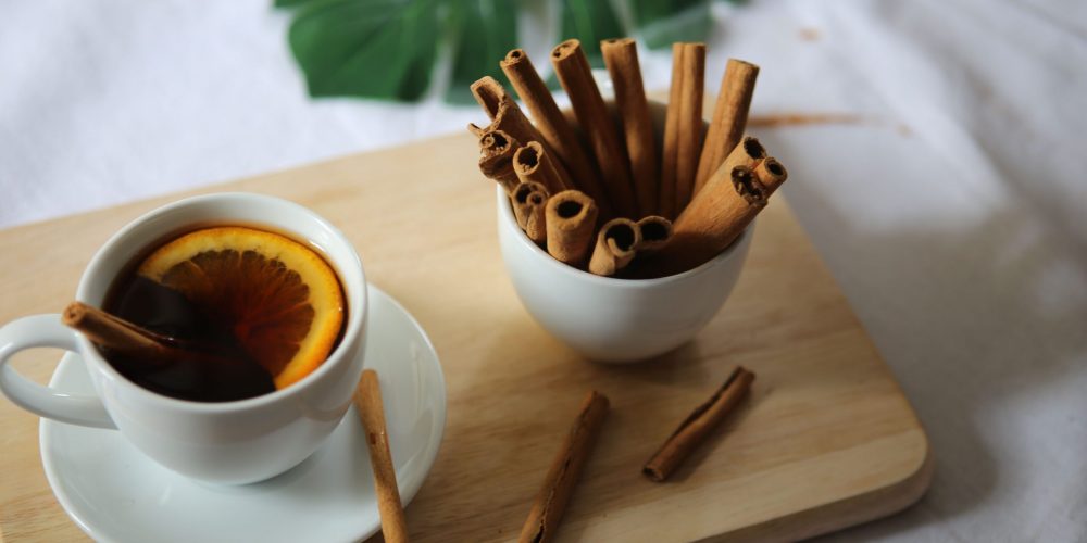 Spiced mulled apple cider in a white cup with an orange slice, beside a bowl of cinnamon sticks