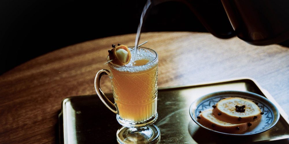 Warm spiced buttered rum in a glass mug with a cinnamon stick, served on a tray