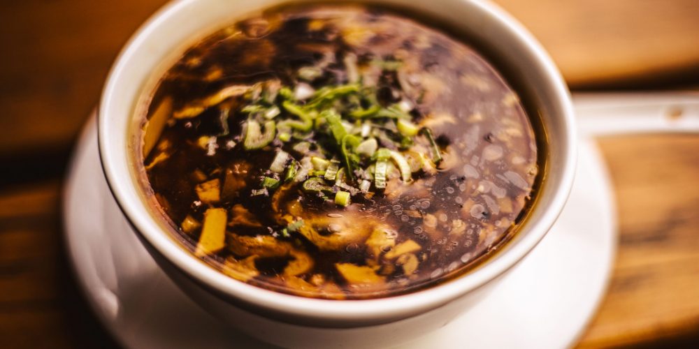 Appetizing hot and sour soup in a bowl garnished with fresh herbs.