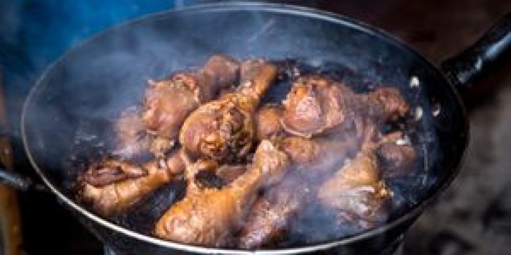 Close-up of juicy smoked chicken drumsticks cooking in a pan, creating mouthwatering steam.