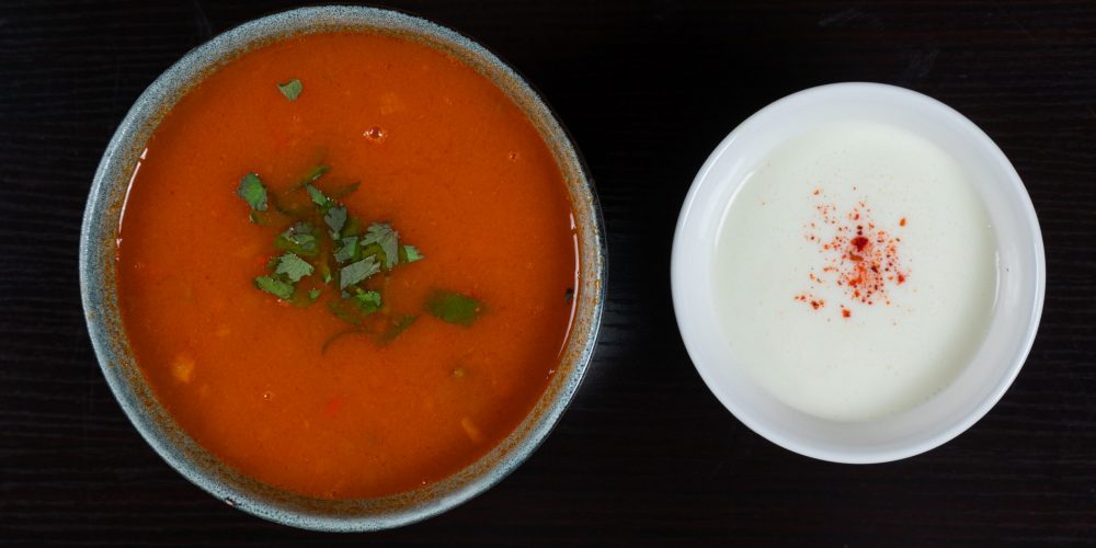 A bowl of tomato soup garnished with cilantro, served alongside yogurt and paprika.