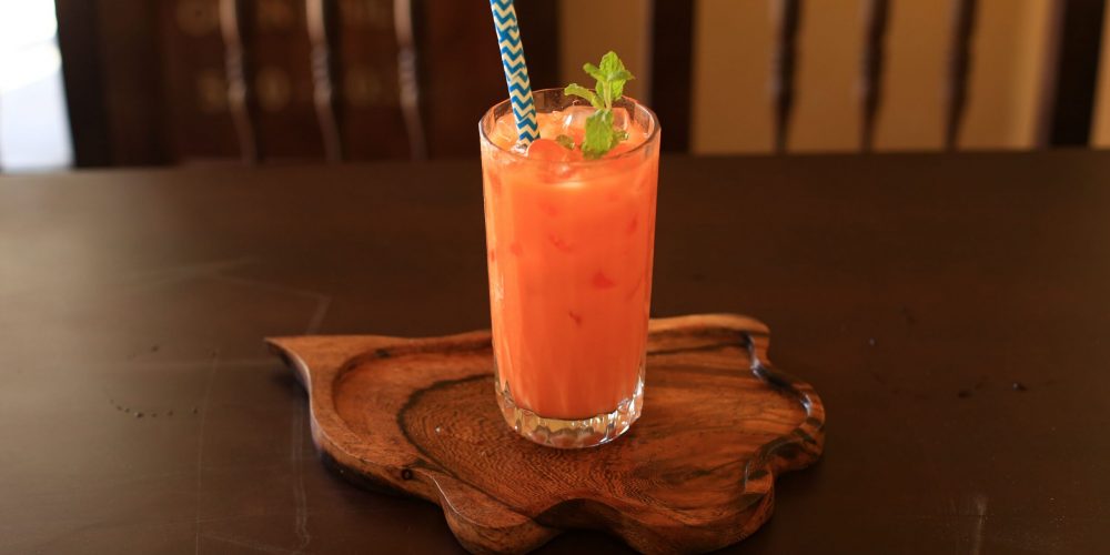 Tall glass of orange Thai iced tea over ice with a mint garnish on a carved wooden tray