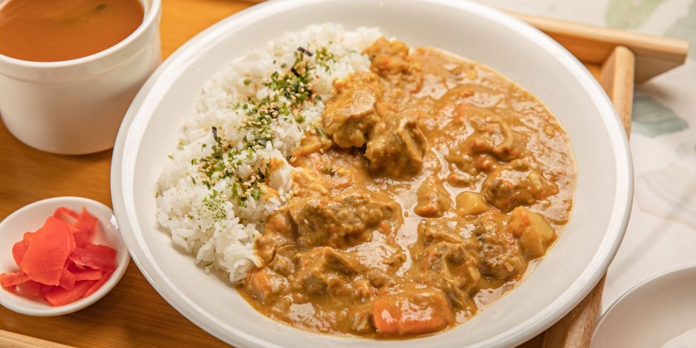 A savory Japanese curry with rice, served with soup and pickles on a wooden tray.