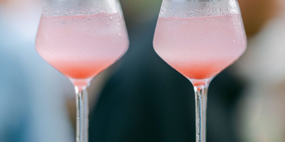 Two pink lychee cocktails garnished with whole lychees, served on a wooden tray