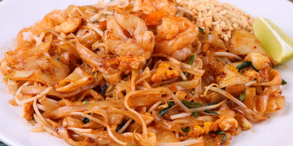 Close-up of shrimp pad thai with lime and peanuts on a white plate, perfect for food lovers.