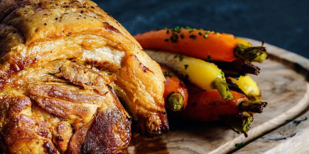 Delicious roast pork served with colorful carrots on a wooden board.