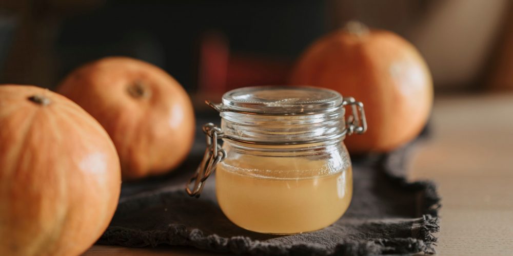 Homemade pumpkin spice syrup in a glass jar beside small pumpkins