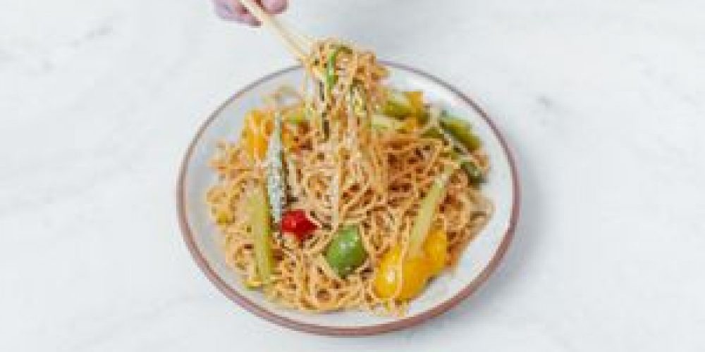 Delicious Asian noodles with colorful vegetables and chopsticks on a bright table.