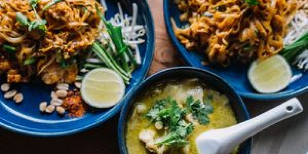 Close-up of delicious Asian noodles and creamy green curry, garnished with fresh herbs.