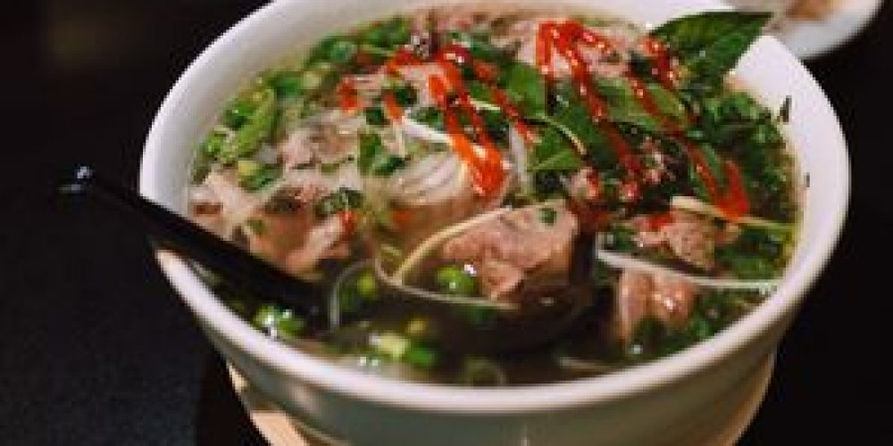 Delicious bowl of traditional Vietnamese pho garnished with fresh herbs and spicy sauce.