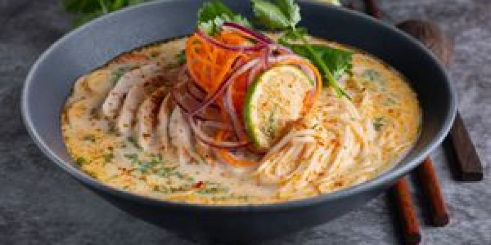 Delicious creamy noodle soup garnished with vegetables and spices. Perfect fusion dish for food lovers.