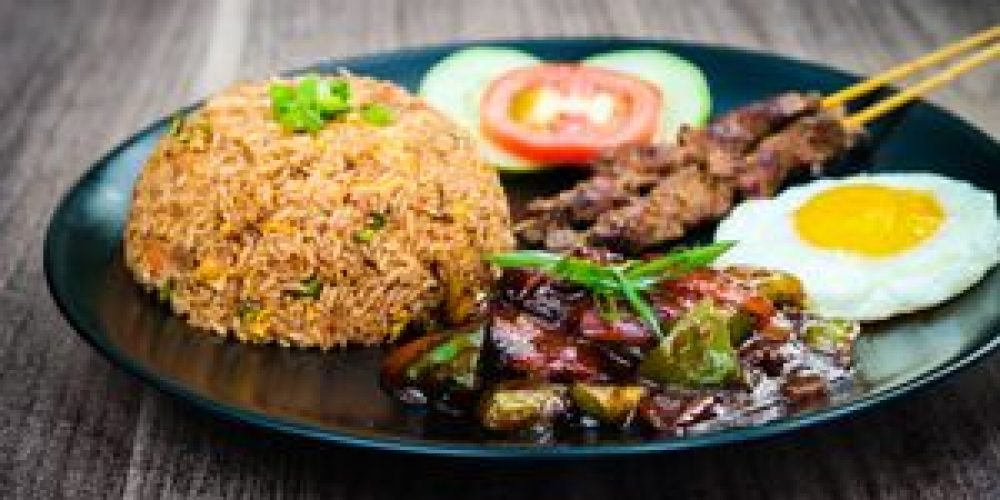 Appetizing Nasi Goreng served with satay, fried egg, and vegetables on a black plate.