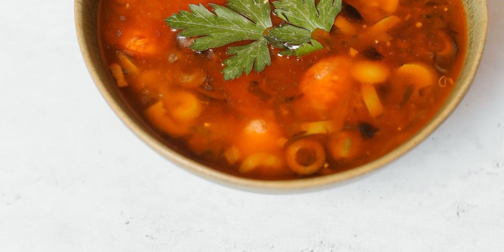 A bowl of minestrone soup with pasta, beans and vegetables in tomato broth, garnished with parsley and served with bread.